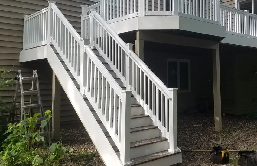 L-shaped deck stairs with white vinyl railings connecting two-story deck to yard