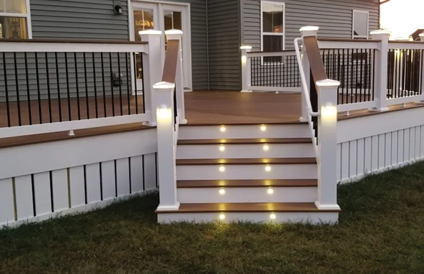 Recessed LED stair riser lights illuminating composite deck stairs with white railing posts