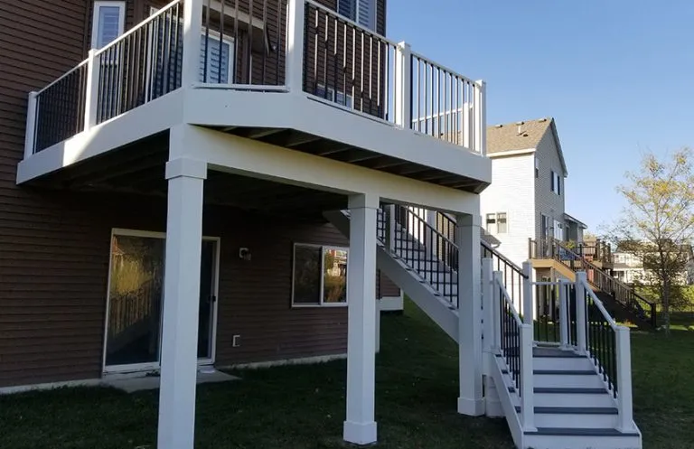 Second-story deck with white composite posts and black aluminum balusters against brick home